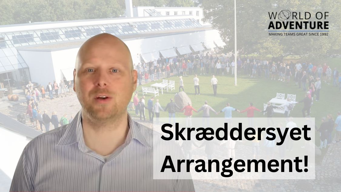 Billedet viser en person, der står foran en baggrund med en stor gruppe mennesker, der deltager i en udendørs teambuilding-aktivitet. Personen i forgrunden taler og ser ud til at præsentere eller forklare noget om arrangementet. Teksten "Skræddersyet Arrangement!" er tydeligt placeret på billedet, hvilket antyder, at aktiviteterne kan tilpasses specifikke behov og ønsker.